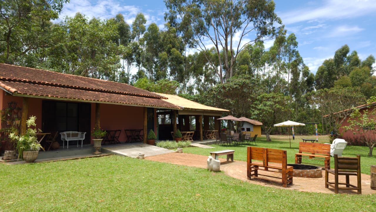Área externa do Rancho Vovó Lulu com gramado, fogueira e bancos de madeira